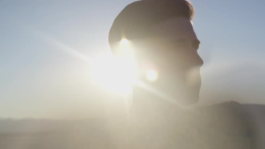 Man standing on a desert looking at the horizon with the sun at his back