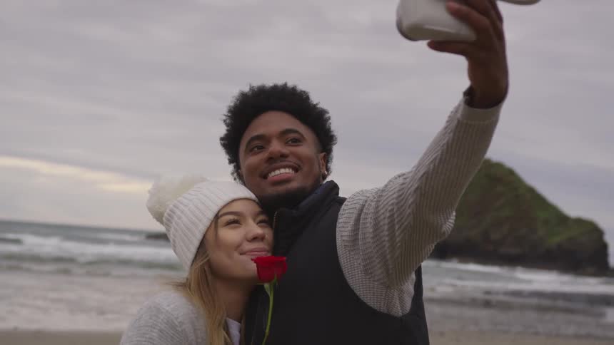 A man and woman pose for a photograph on a beach with a red rose