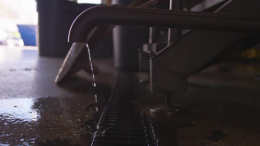 Water dripping out of a stainless steel pipe into a grate in the floor