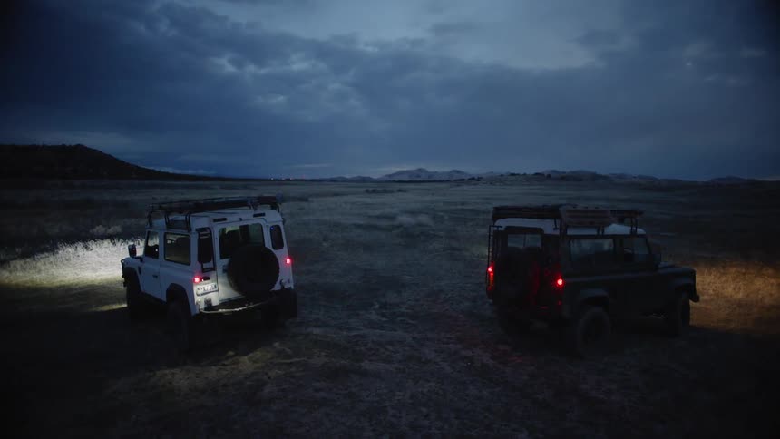 Two cars are parked in a field, and people get out of the car