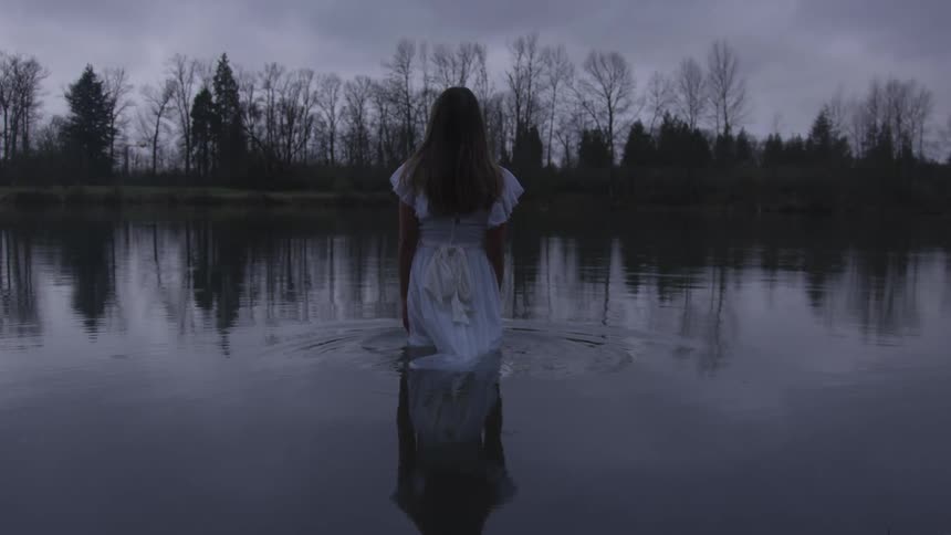 Woman in white dress wades into pond during winter