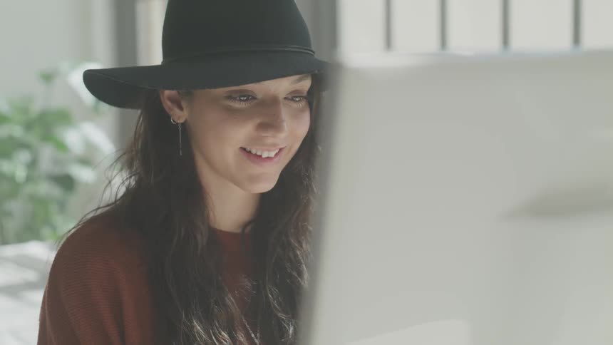 Woman in black hat sits in sunny room in front of canvas