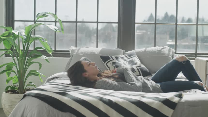 Woman sitting on the side of a bed and then laying back