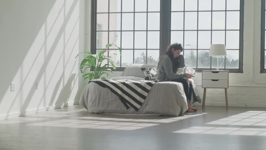 Woman wipes hair out of face while sitting on a bed