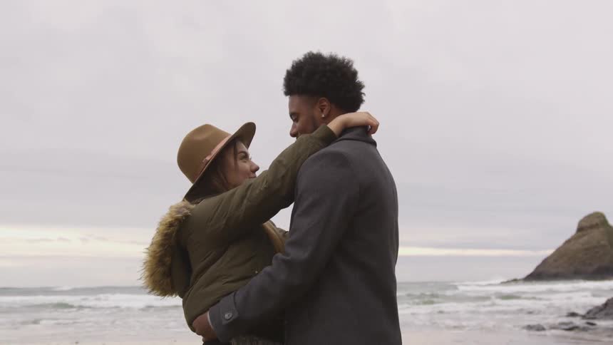 Woman and man holding each other at beach on a cold day