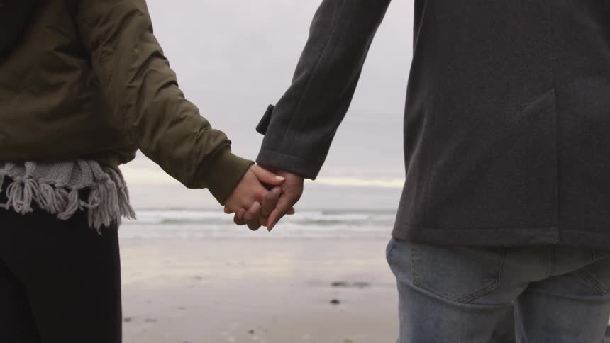 A man and woman hold hands walking on the beach