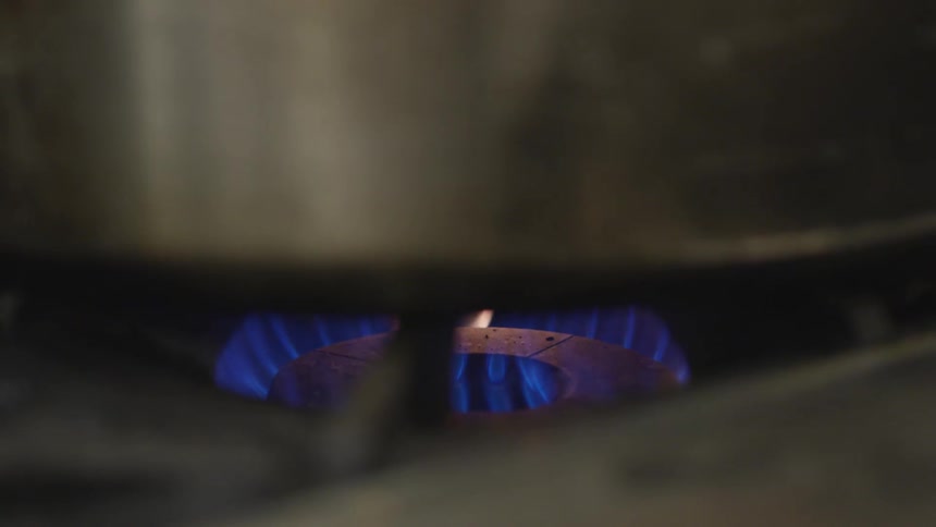 A flame burns on a stove top beneath a pot