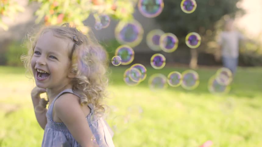 A little girl laughs as bubbles are blow towards her