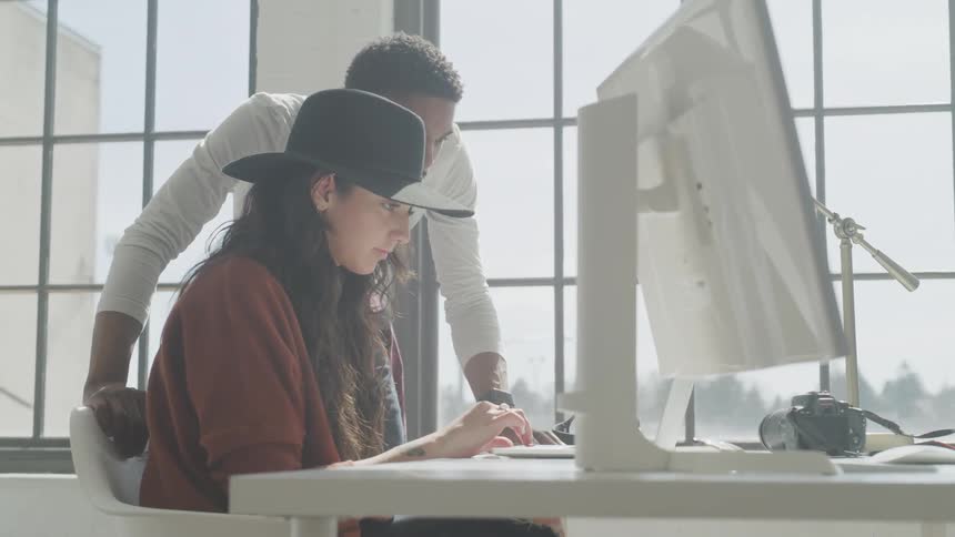 A man leans over a woman's chair and points as she works on a computer