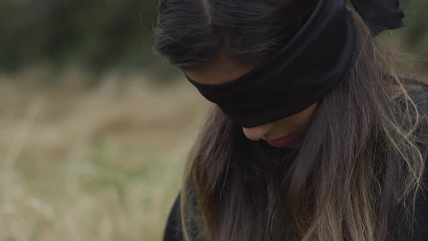 Blindfolded woman kneels in a field
