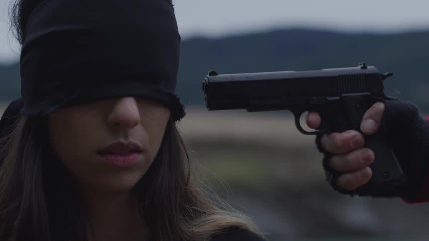 A blindfolded woman has a gun pointed at her head