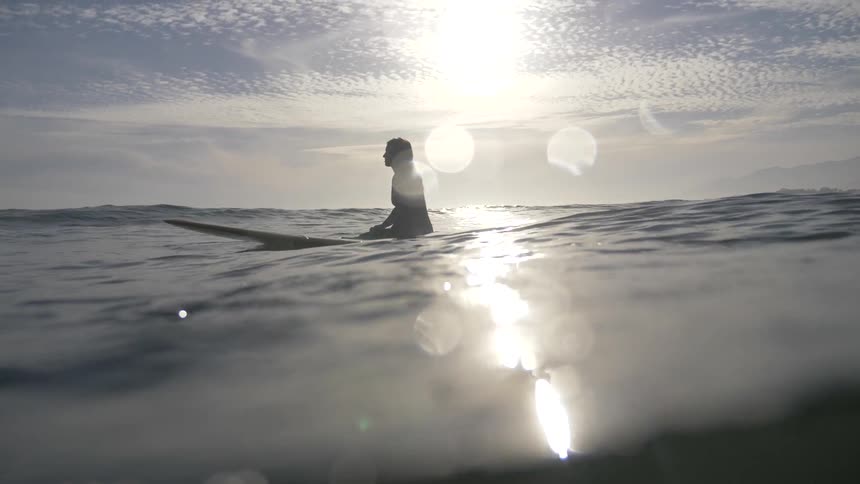 A surfer sits on her board in the ocean on a sunny day