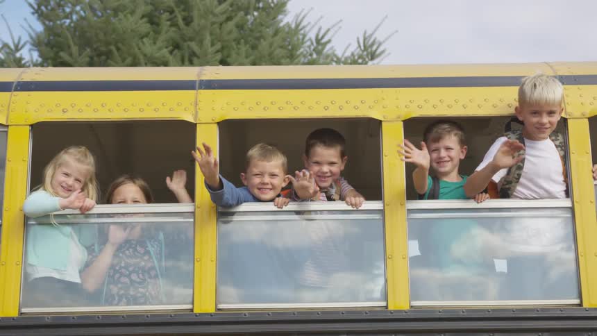 Six kids waving out the windows from a school bus
