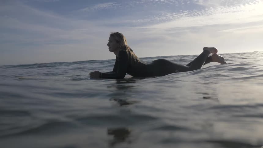 A surfer lays belly down on her board in the ocean