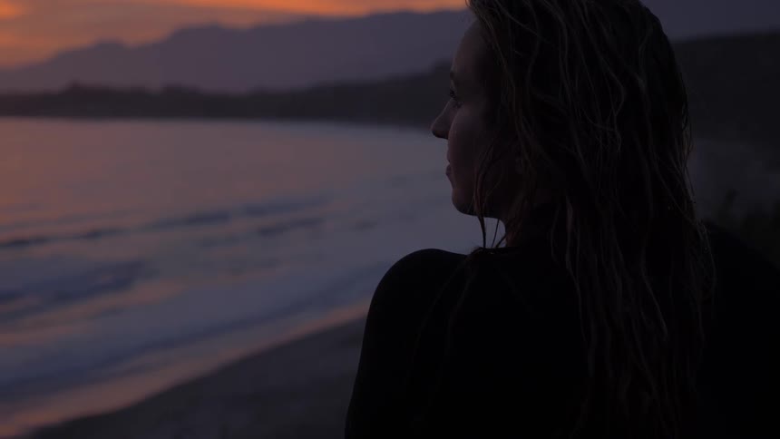 Woman watches sunset from beach shore