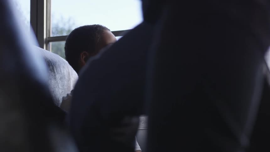 A little boy sits on a bus looking out a window