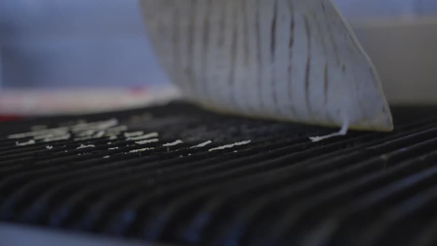 Person takes a tortilla off a grill