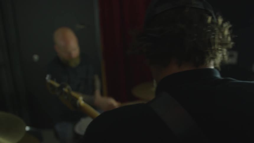 A man plays a guitar while another plays the drums