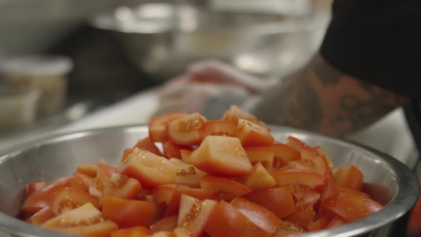 A man cooking is placing cut tomatoes in a bowl