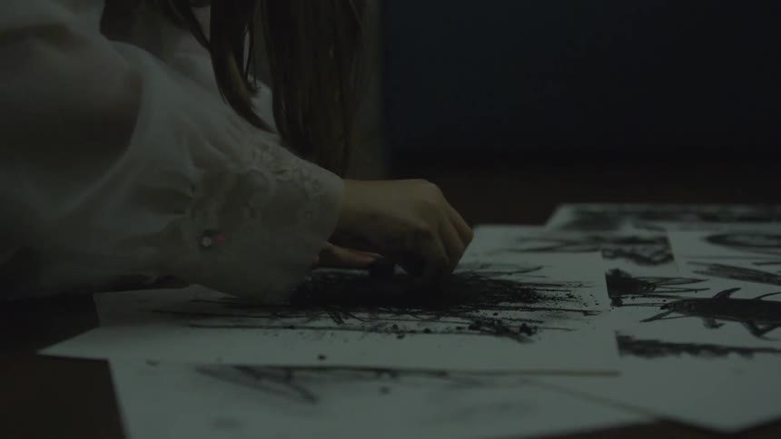 A girl rubs charcoal on paper inside in a dark room
