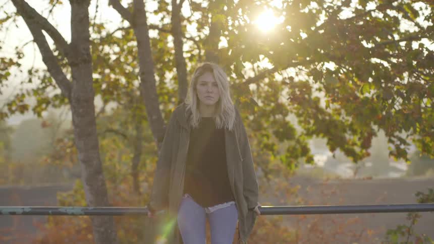 A woman sits on a handrail outside on a sunny autumn day