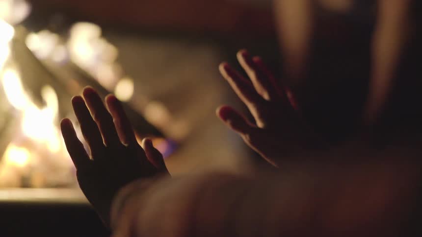 A person warms their hands next to a campfire at night