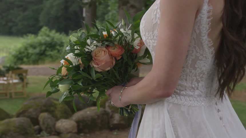 A woman in the outdoors wearing a wedding dress and talking a step while holding a bouquet with both hands