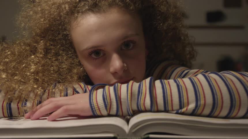 A curly haired girl rests on her arms on a large book