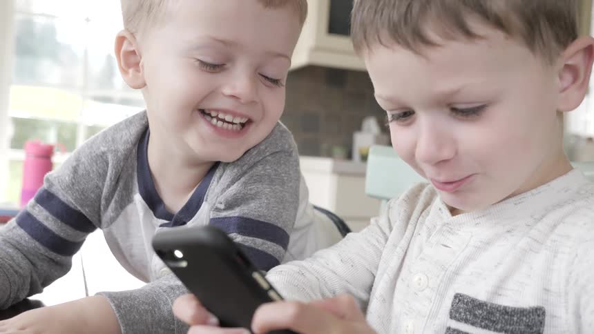 Two small children laughing at a smartphone
