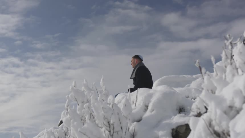 A man sits on snow and looks out into the distance