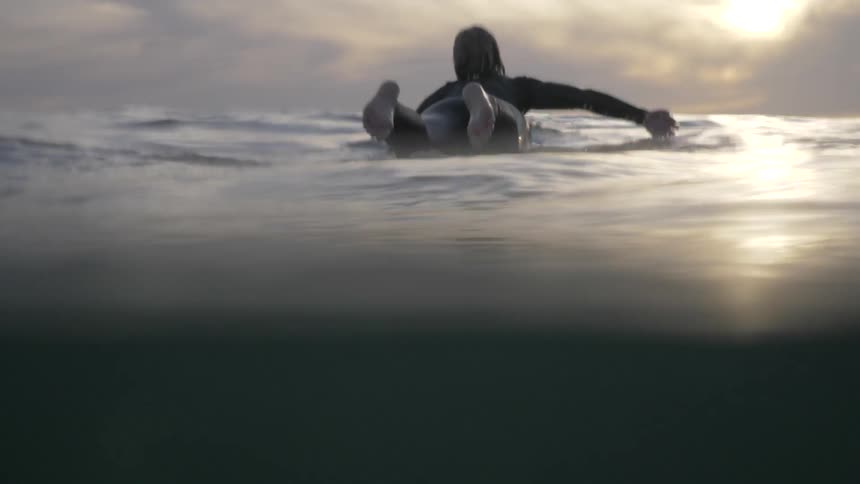 A woman on a surfboard paddles out into the ocean\