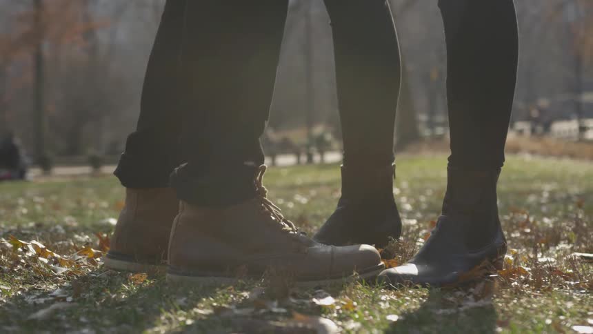 Two pairs of boots holding people are standing close together in a park