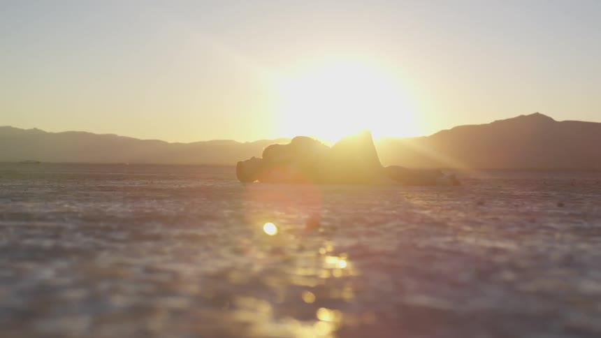 A woman lying on top of a man on the sand at sunset
