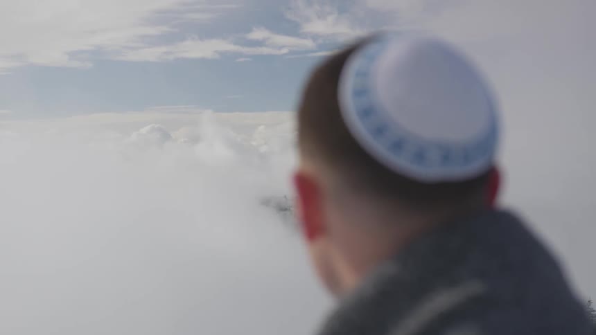 A man wearing a yamaka looks at clouds in the sky