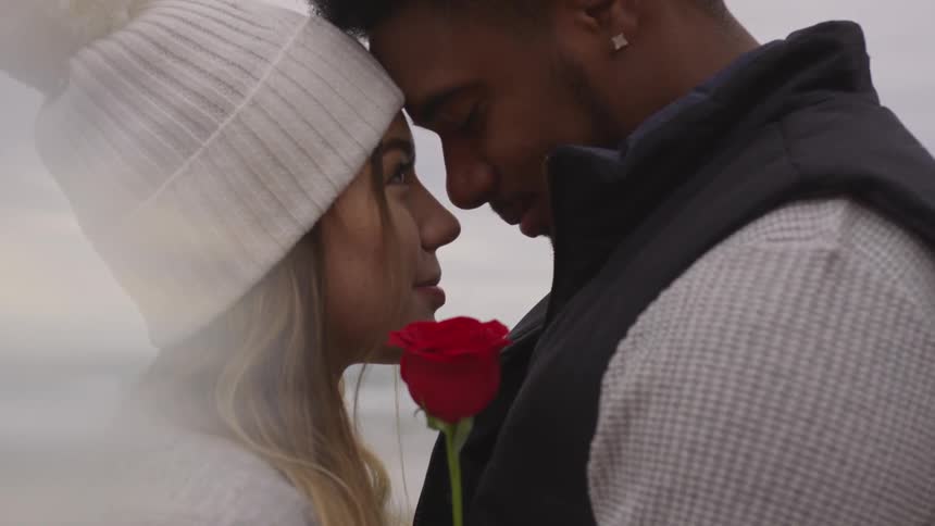 A man and woman gaze into each other's eyes while holding a red rose