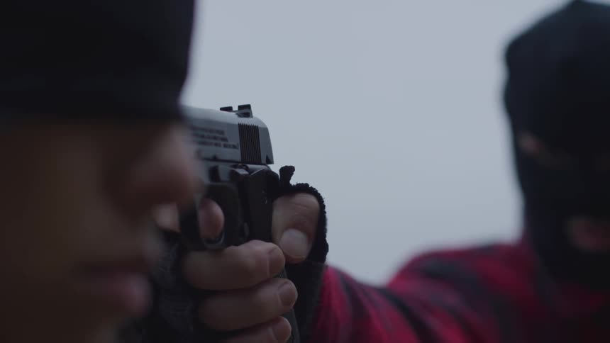 A masked man holds a gun to a blindfolded woman