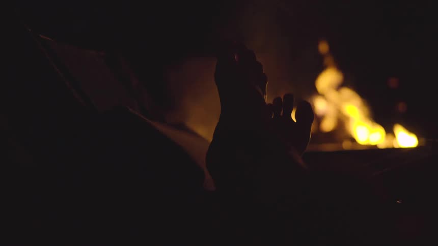 Man's feet silhouetted by the flames on a fireplace