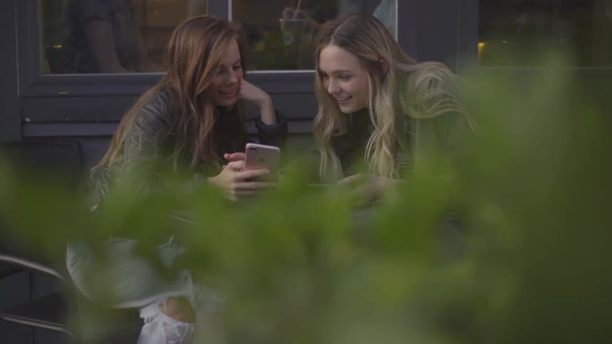 Two women sitting outside laughing and looking on a phone