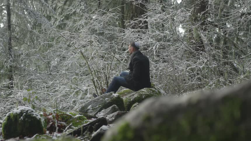 A man sits on rocks in a snow covered forest