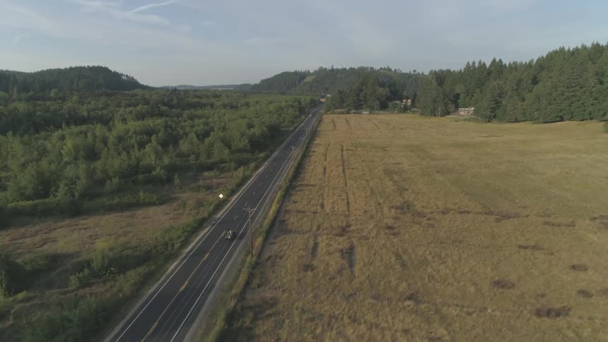 A car driving down an empty road through rural fields