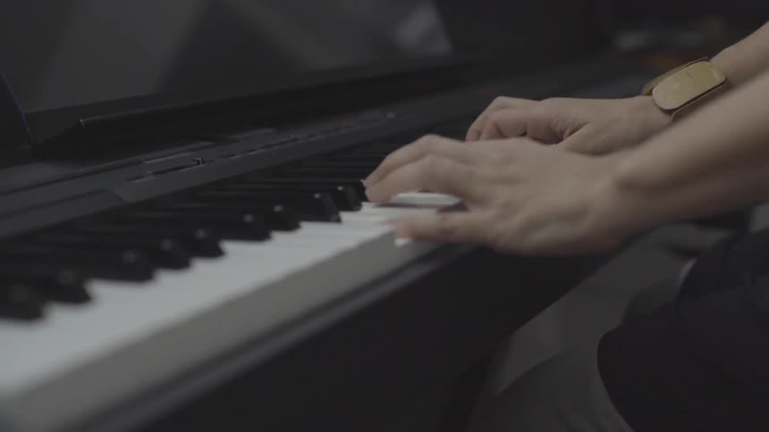 A piano is being played by a woman indoors with minimal lighting on the black piano