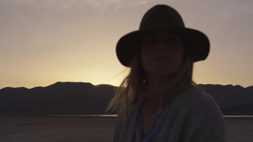 Girl wearing hat stands in the desert at sunset