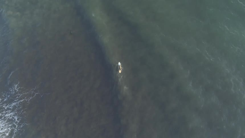 Someone paddles a surfboard far below