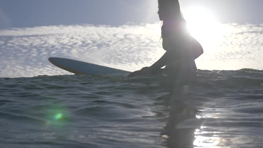 Woman sits on her surfboard in the sea during the day