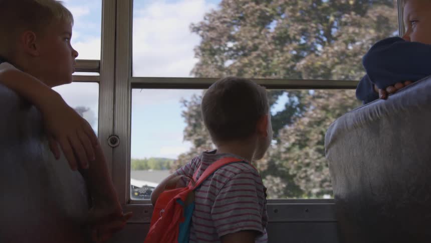 The children look out the window of the bus as it travels