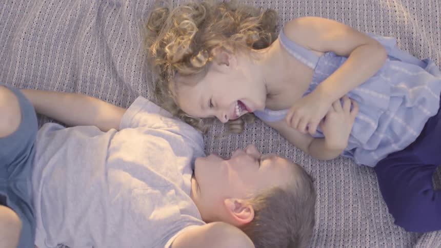 Two children lay on their backs on a sheet smiling at each other