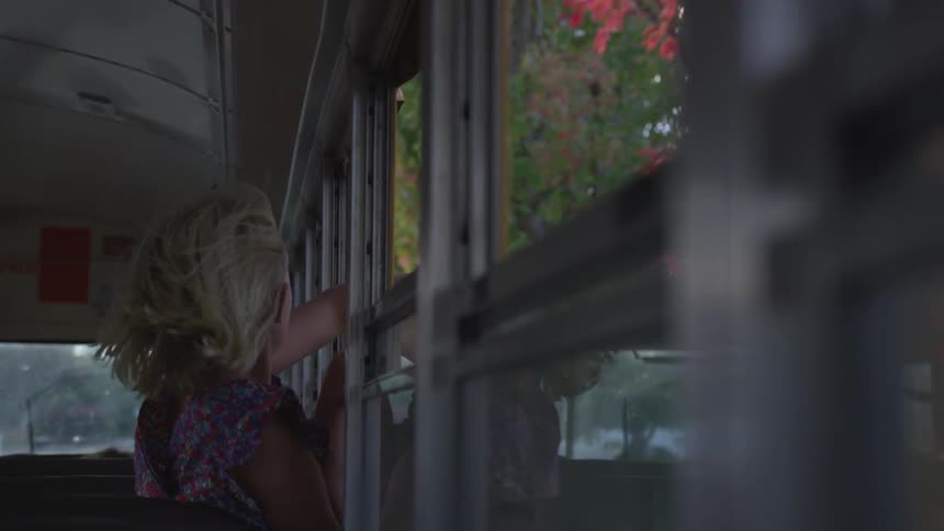 The wind blows a child's hair through the open window of a school bus