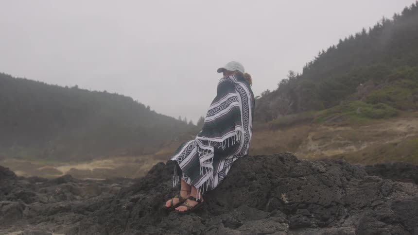 Woman sitting on lava rock wrapped in a blanket