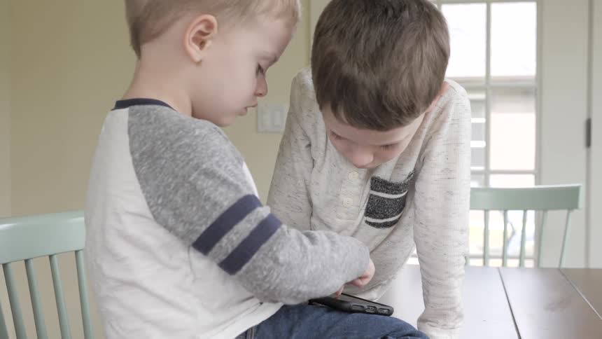 Two boys sit on a table playing with a cellphone