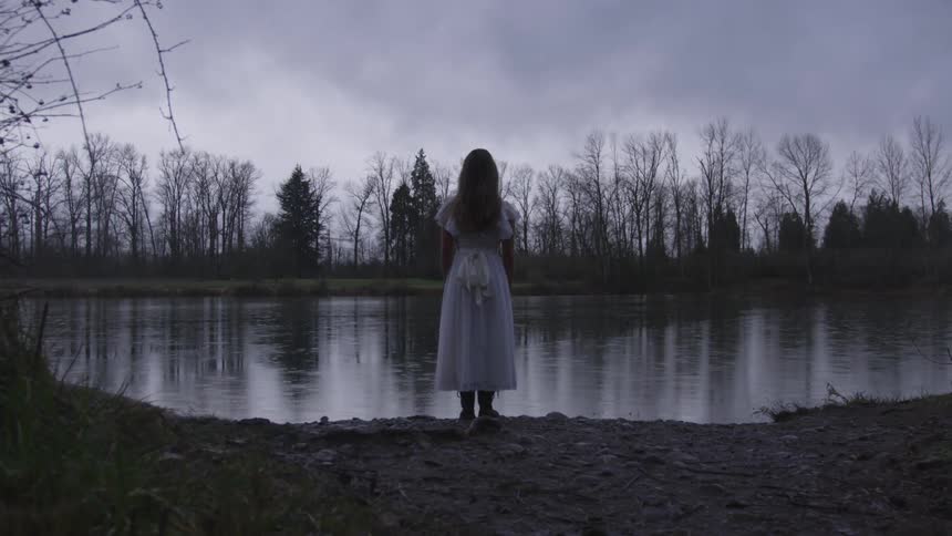 A girl in a dress stands at the edge of a river
